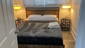 Un dormitorio con una cama, dos lámparas de noche, un ventanal con persianas y una puerta.
