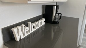 Una encimera de cocina con una cafetera negra y un letrero blanco que dice 'Welcome'.