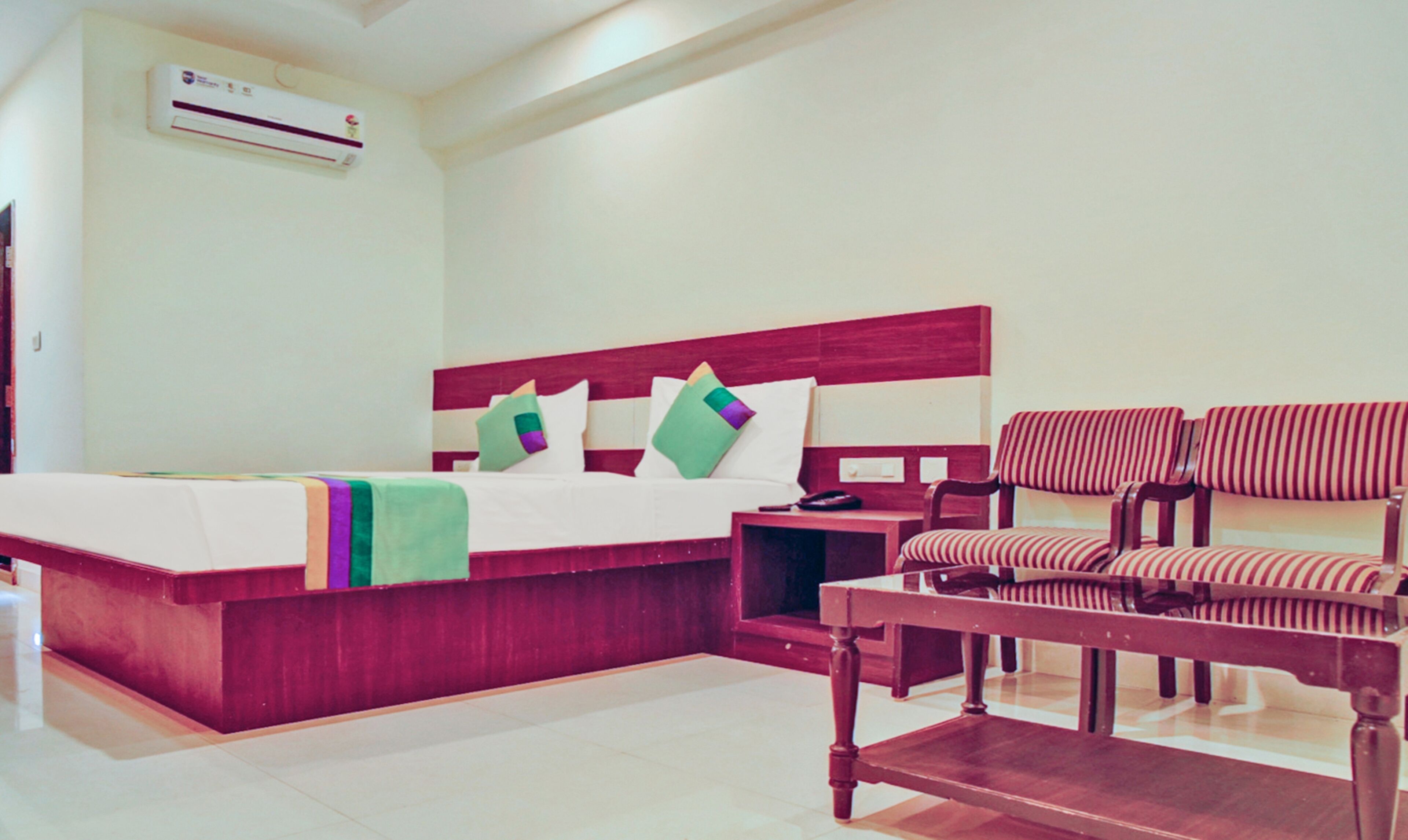 A hotel room with a bed, a desk, and two striped armchairs.