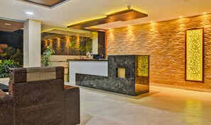A modern reception area with a stone wall, a reception desk, and a seating area with a brown sofa. - Treebo Trend Hotel Subashree (Coimbatore)