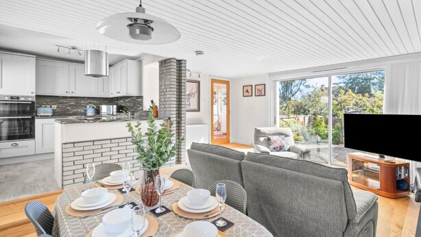A modern kitchen with white cabinets, a brick accent wall, and a dining area with a table set for six. - The Albatross - 3 bed Carnoustie Classic (Angus)