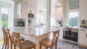 A modern kitchen with white cabinets, a granite countertop, and a central island with bar stools. - 2 Minute Walk to Beach; Access to Community Pool and Pickle Ball, Basketball & Tennis Courts (Isle of Palms)