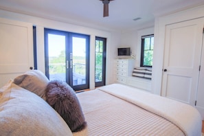 A bedroom with a bed, a dresser, a television, and a sliding glass door leading to a balcony. - Newly Constructed, Custom Built Home w/ Mesmerizing Marsh Views, 2 Master Suites & Outdoor Spaces (Kiawah Island)