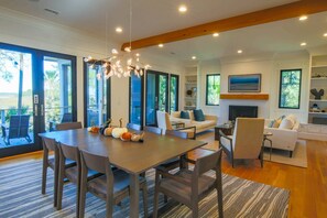 A spacious living area with a wooden dining table, comfortable seating, and large windows offering views of the outdoors. - Newly Constructed, Custom Built Home w/ Mesmerizing Marsh Views, 2 Master Suites & Outdoor Spaces (Kiawah Island)