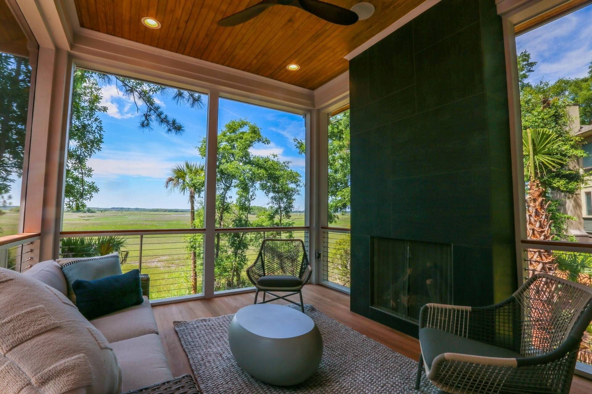 A spacious room with a large window offering a view of a green landscape. There is a sofa, two chairs, and a round table.
