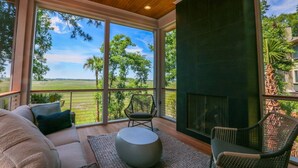 A spacious room with a large window offering a view of a green landscape. There is a sofa, two chairs, and a round table. - Newly Constructed, Custom Built Home w/ Mesmerizing Marsh Views, 2 Master Suites & Outdoor Spaces (Kiawah Island)