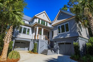 A two-story house with a front porch, a staircase leading to the second floor, and a garage. - Newly Constructed, Custom Built Home w/ Mesmerizing Marsh Views, 2 Master Suites & Outdoor Spaces (Kiawah Island)