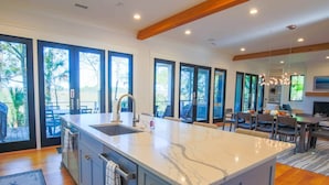 A modern kitchen with a large island, built-in appliances, and large windows offering views of the outdoors. - Newly Constructed, Custom Built Home w/ Mesmerizing Marsh Views, 2 Master Suites & Outdoor Spaces (Kiawah Island)