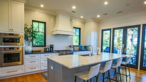 A modern kitchen with white cabinetry, stainless steel appliances, and a large island with bar stools. - Newly Constructed, Custom Built Home w/ Mesmerizing Marsh Views, 2 Master Suites & Outdoor Spaces (Kiawah Island)