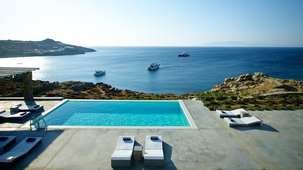 Un espace piscine avec des chaises longues et une vue sur la mer et les bateaux.