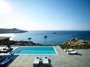A pool area with lounge chairs and a view of the sea and boats. - Serifos (Mykonos)