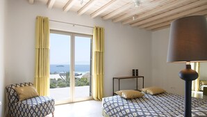 Une chambre à coucher avec un lit, une chaise, une table et une vue sur la mer, visible à travers une grande fenêtre.