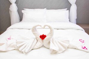 A bed with white bedding and a heart-shaped towel arrangement with a red flower in the center. - Grand Forty Hotel (Ahero)