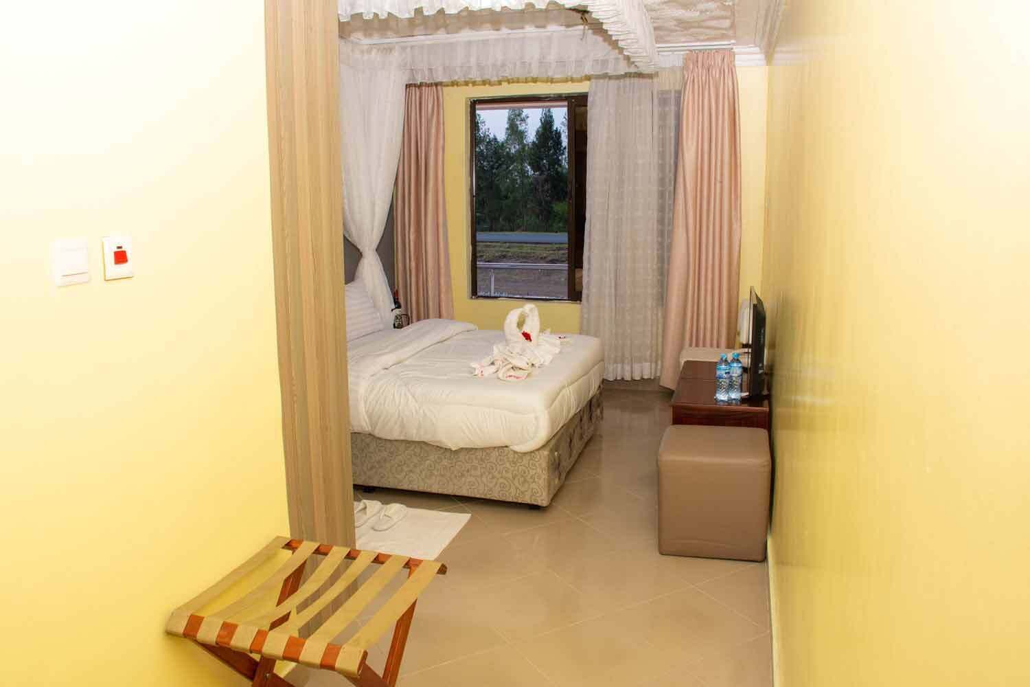 Una habitación de hotel con una cama, una mesita con una botella, una silla y una ventana con cortinas.