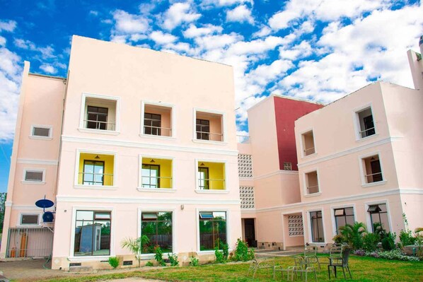 Un edificio a più piani con facciata piatta, ampie finestre e un piccolo giardino con sedie.
