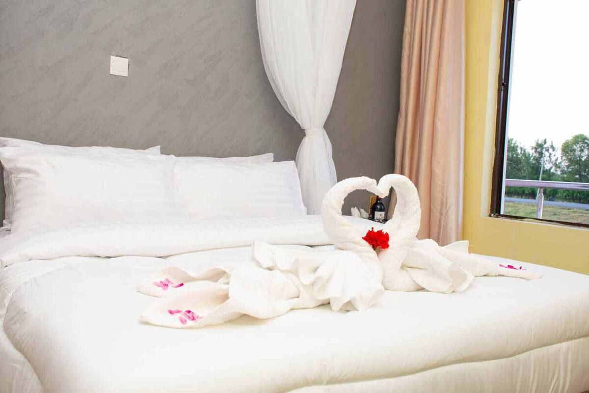 A neatly made bed with white linens and a heart-shaped towel arrangement.