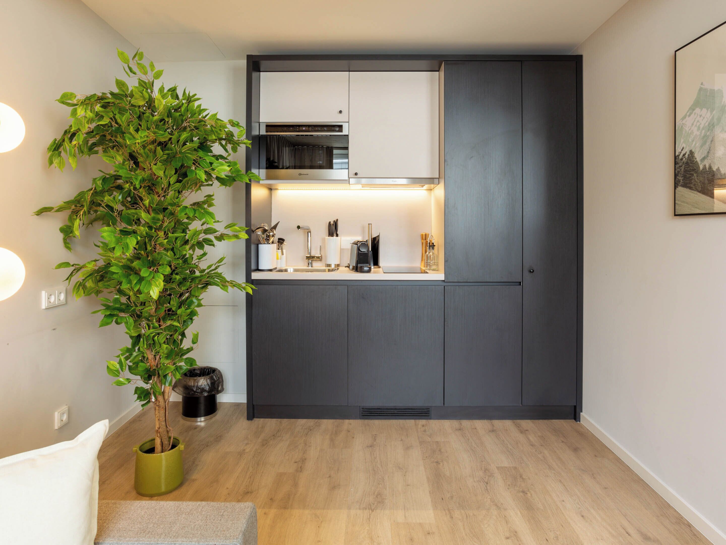 A compact kitchen with dark cabinetry, a built-in oven, and a countertop with various appliances and utensils.
