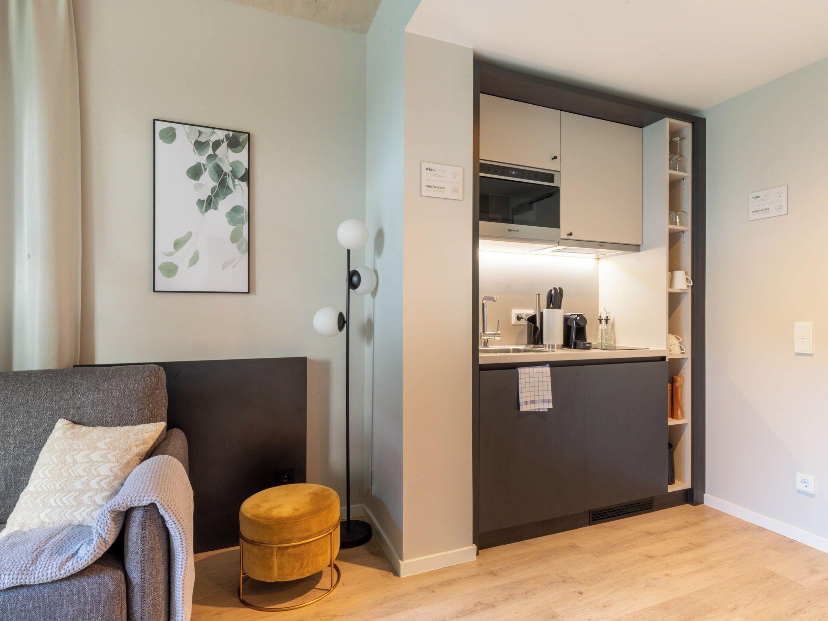 A compact living space with a kitchenette, a sofa, and a small round ottoman.