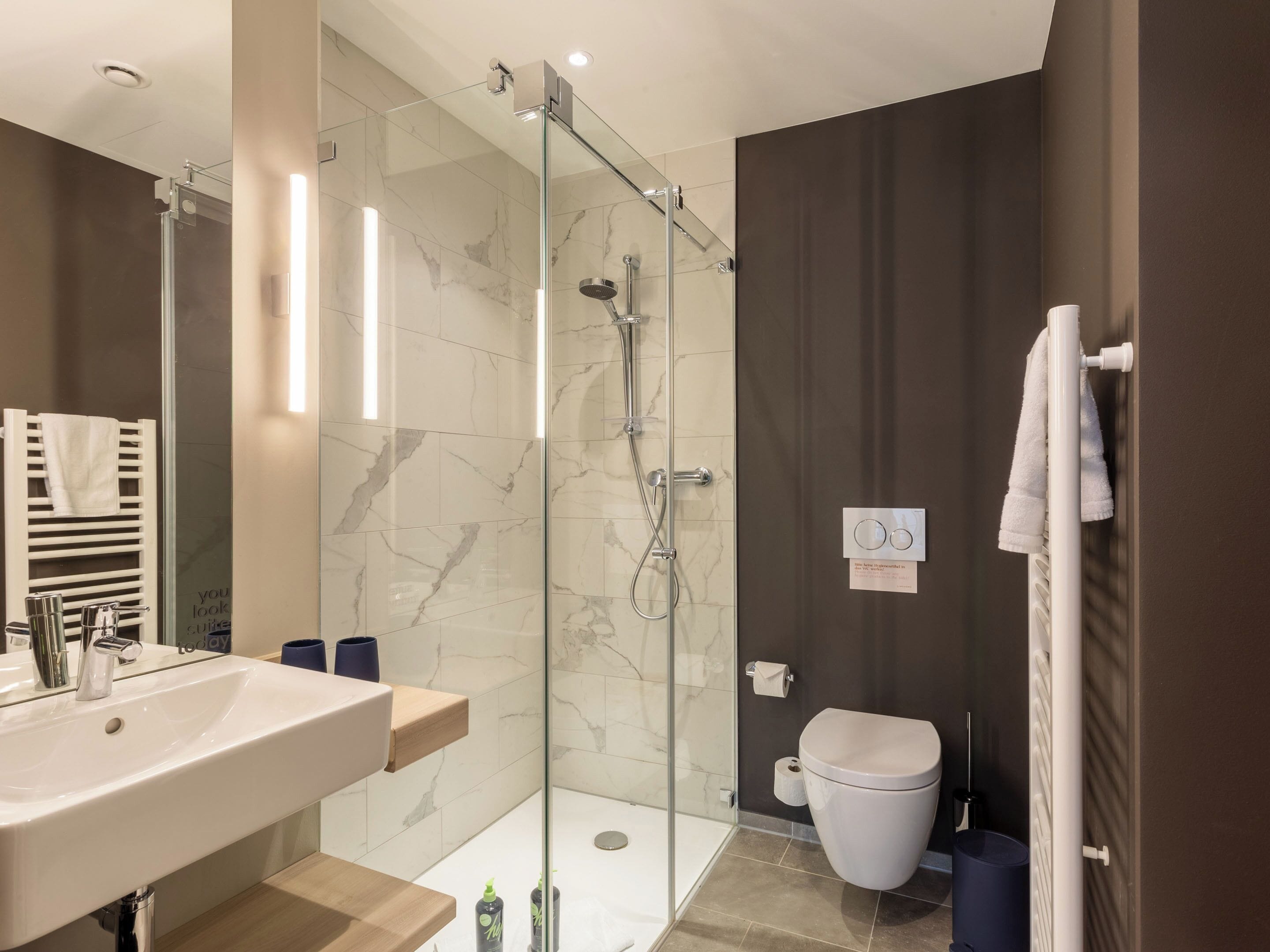 A modern bathroom with a glass-enclosed shower, a white sink, and a toilet.