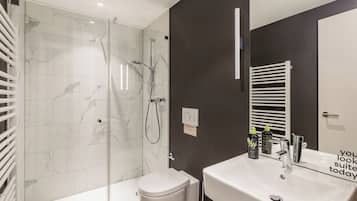A modern bathroom with a glass-enclosed shower, a white toilet, and a large sink with a mirror.
