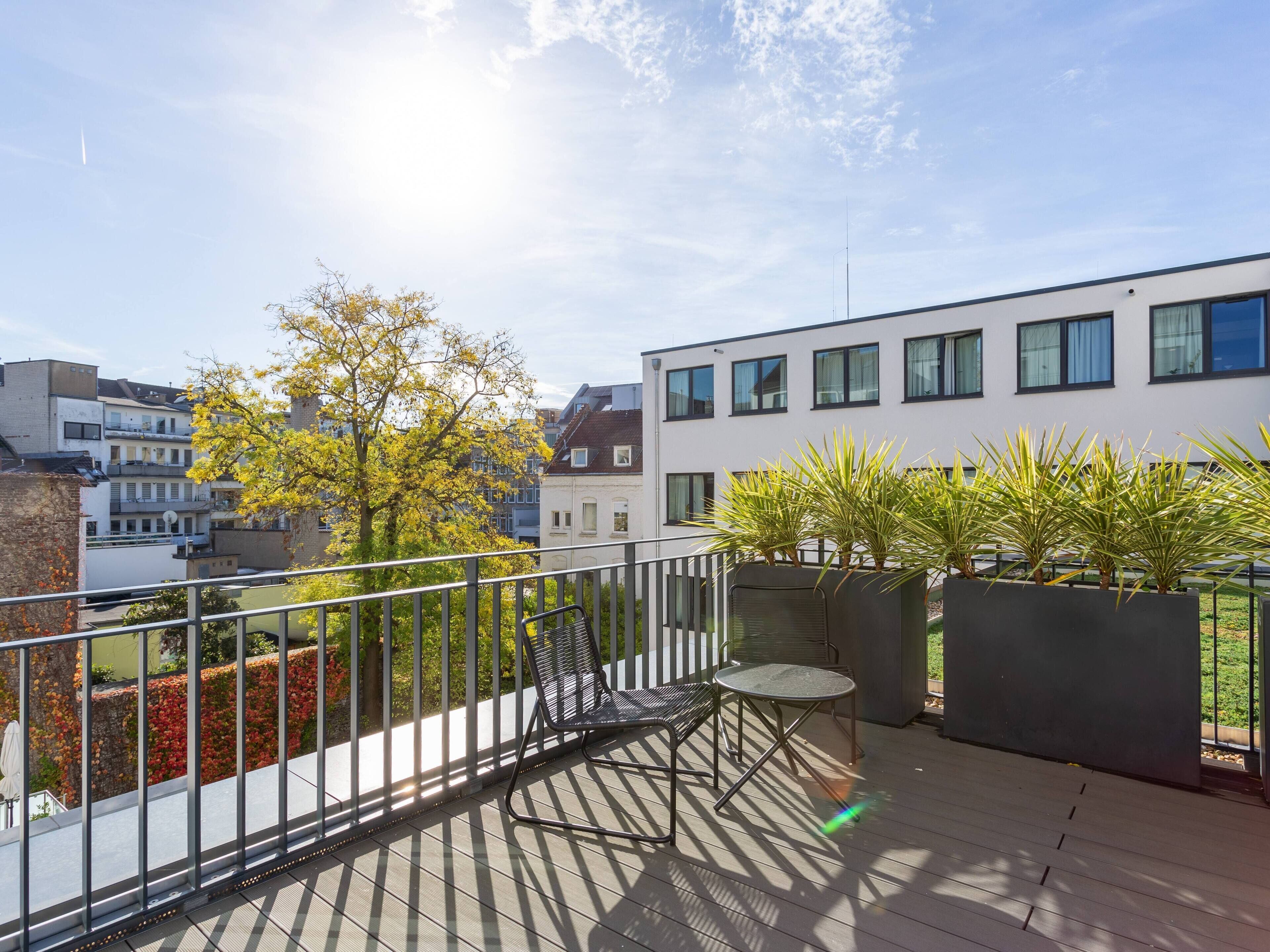 A balcony with a metal chair and table, surrounded by potted plants and a view of buildings.