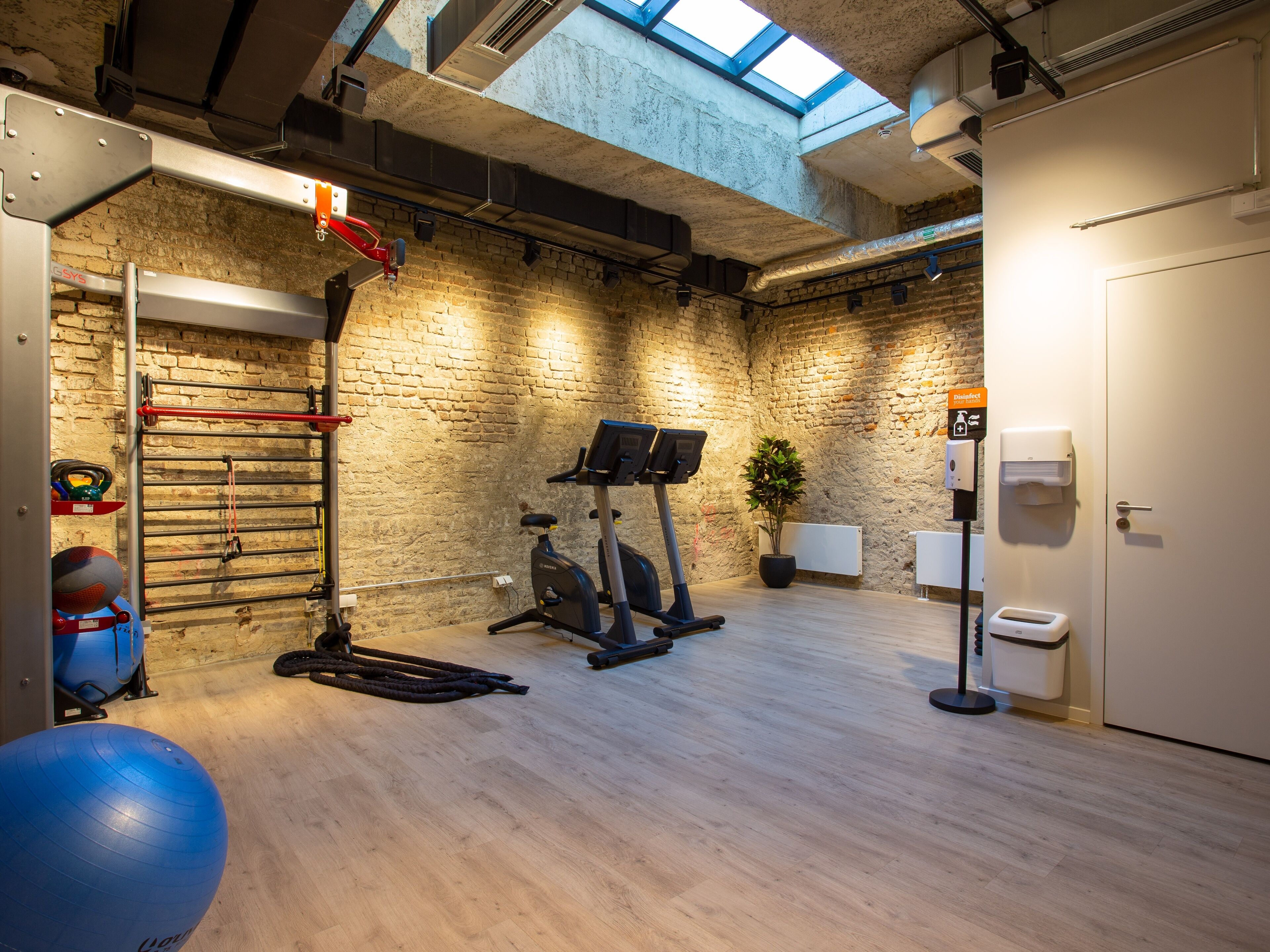 A gym with exercise equipment, a brick wall, a skylight, and a white door.