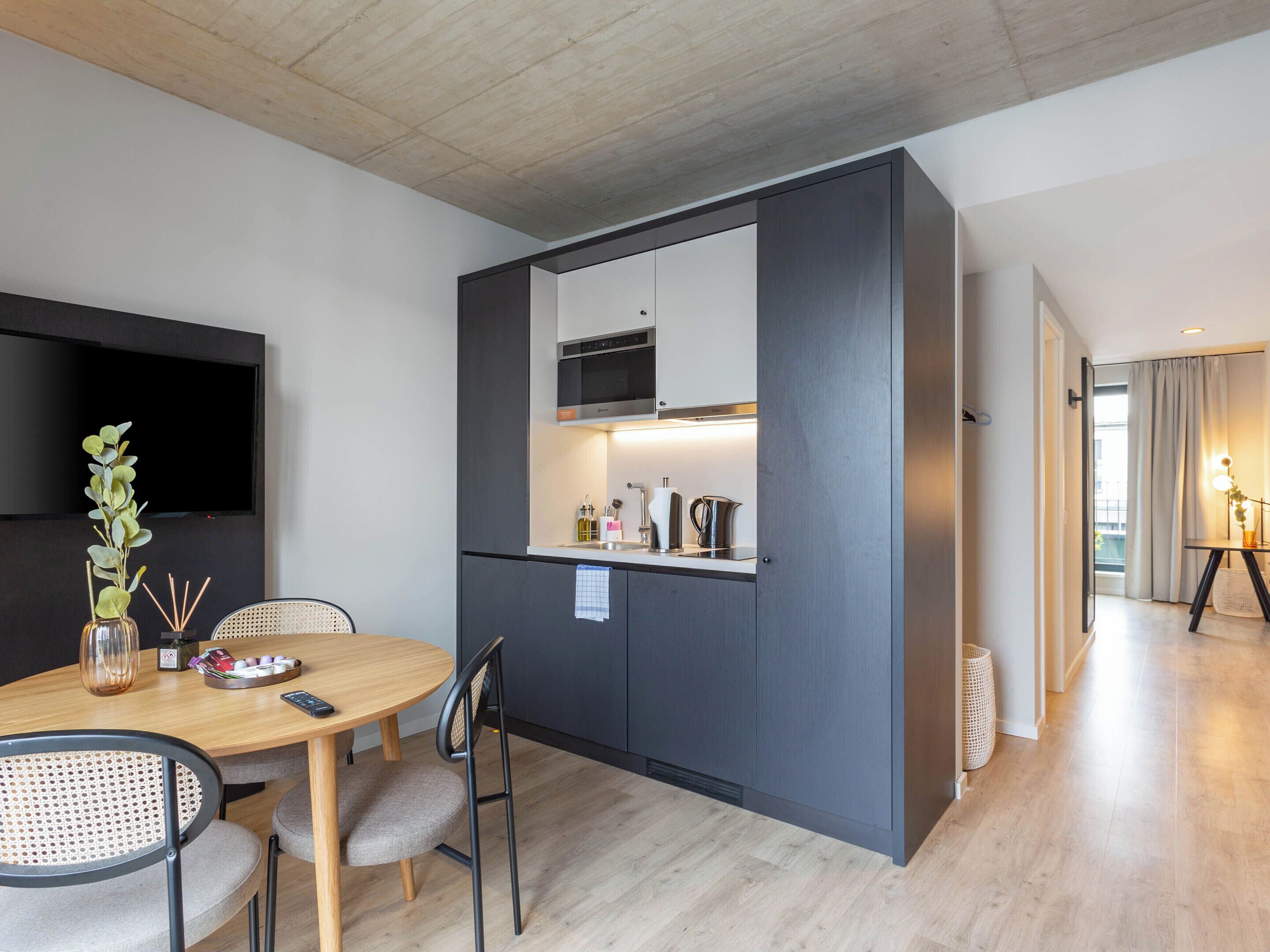 A compact kitchen with modern appliances, a dining area with a wooden table and chairs, and a large mirror above the counter.