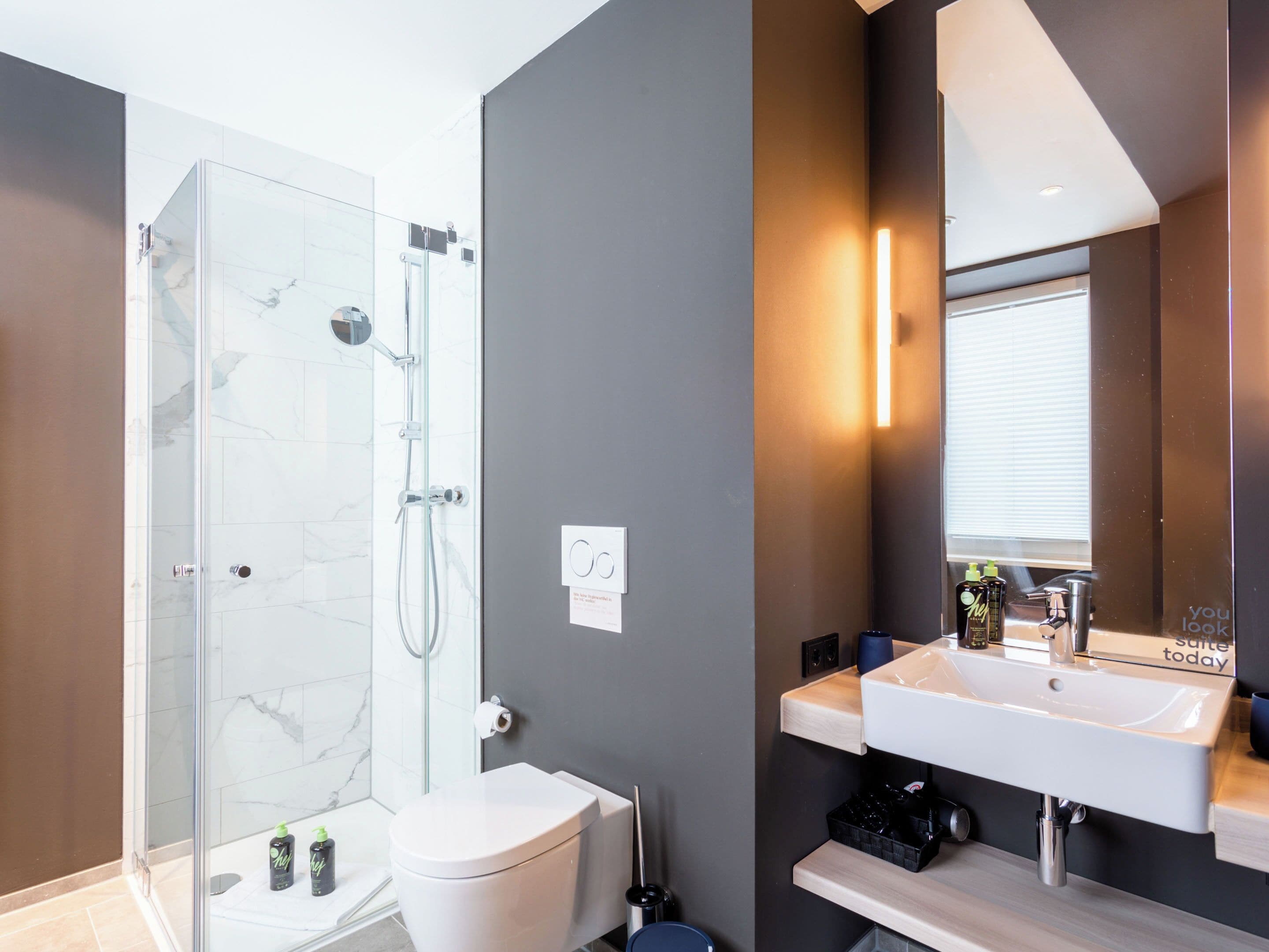 A modern bathroom with a glass-enclosed shower, a white toilet, and a white sink with a mirror above it.