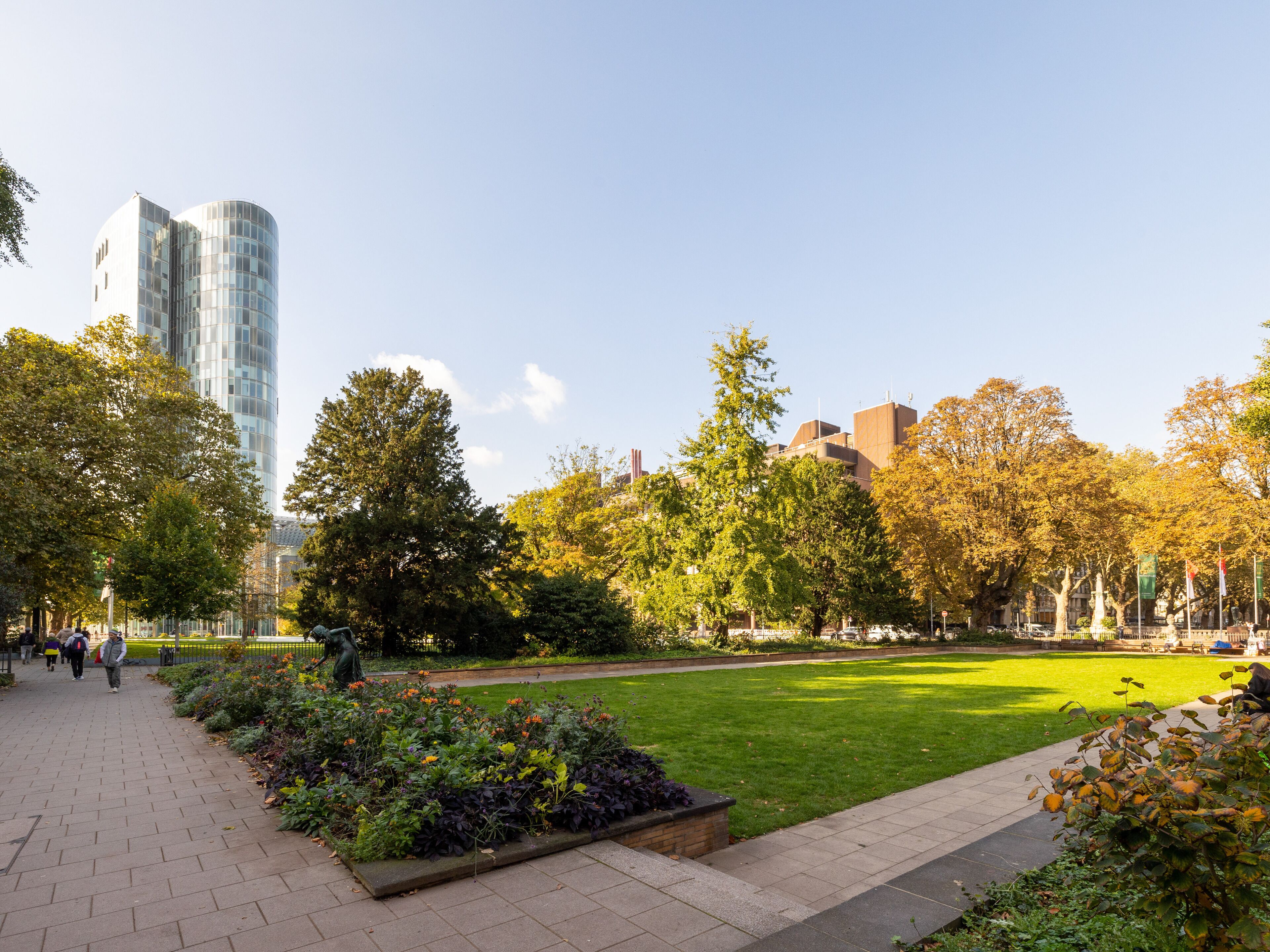 A park with a paved walkway, green grass, and trees.