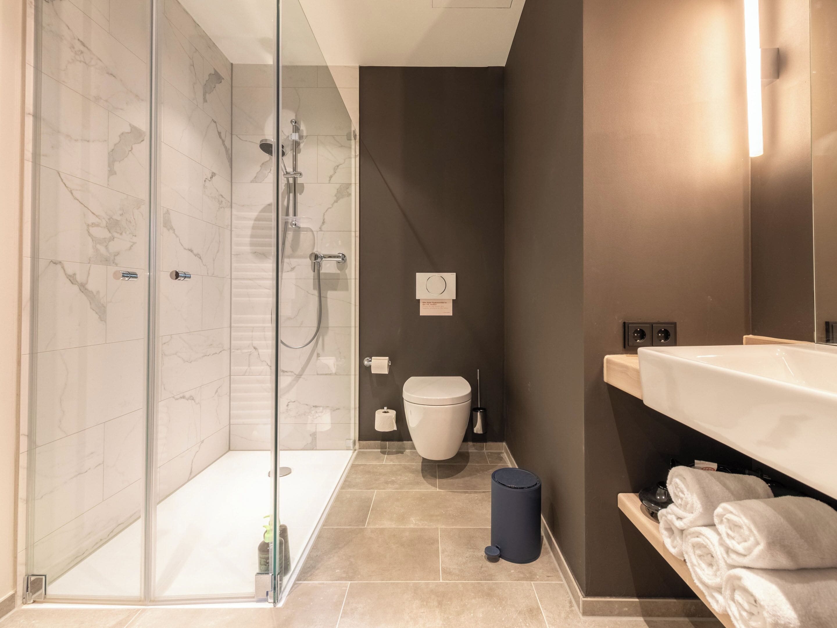 Un bany modern amb dutxa de vidre, un vàter i un lavabo amb barra de tovalloles.