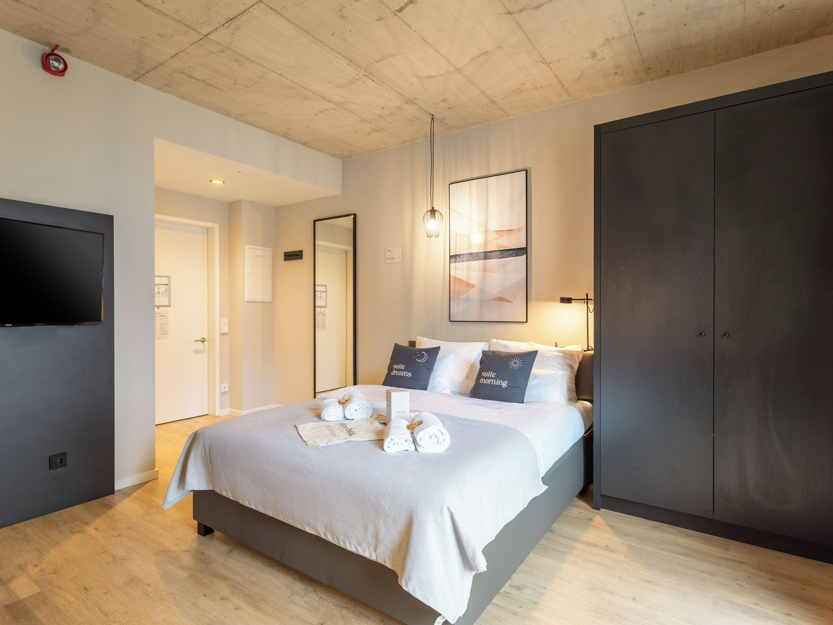 A modern hotel room with a large bed, a flat-screen TV, a wardrobe, and a mirror.