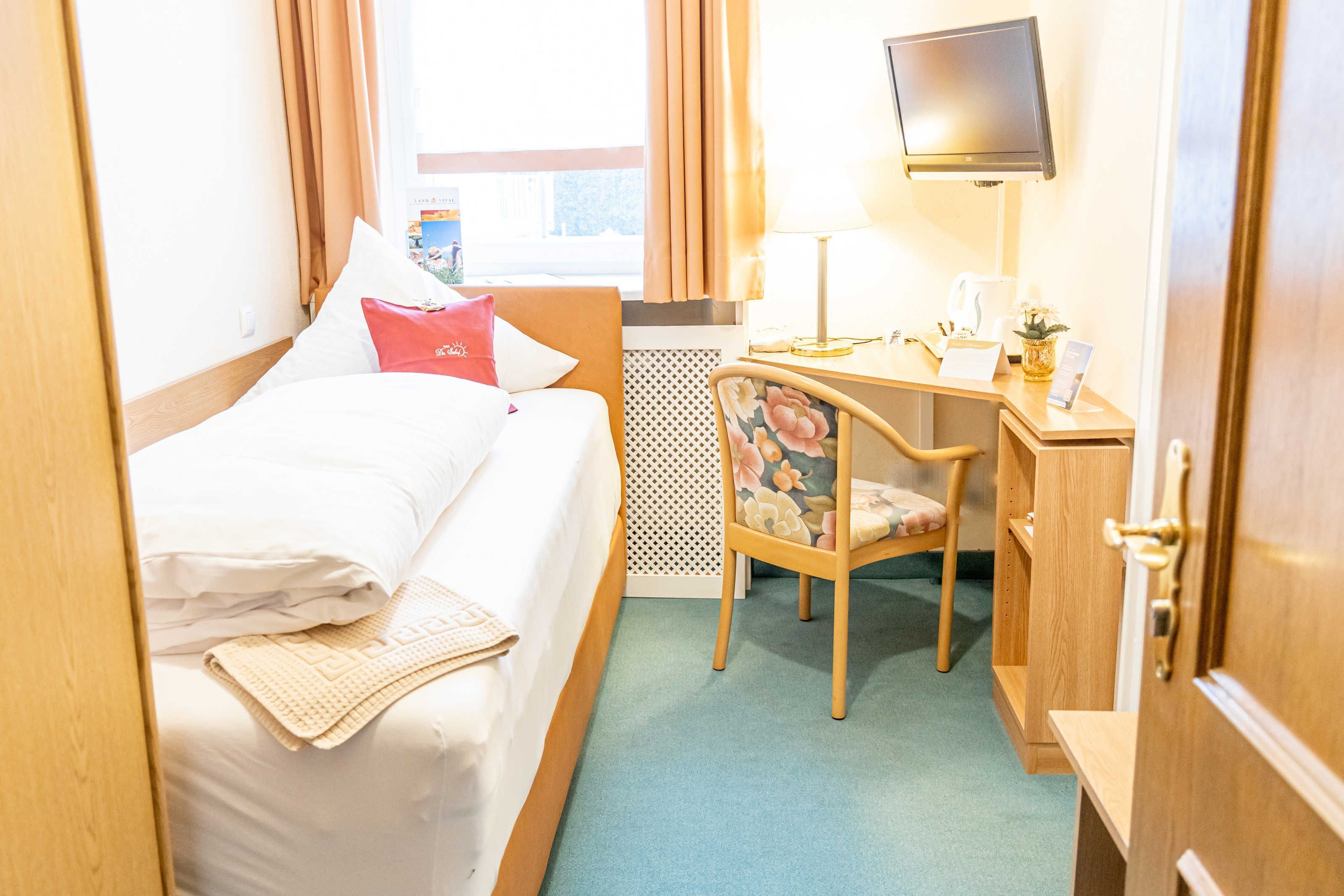 Une chambre d’hôtel équipée d’un lit, d’un bureau, d’une chaise, d’une télévision et d’une fenêtre avec des rideaux.