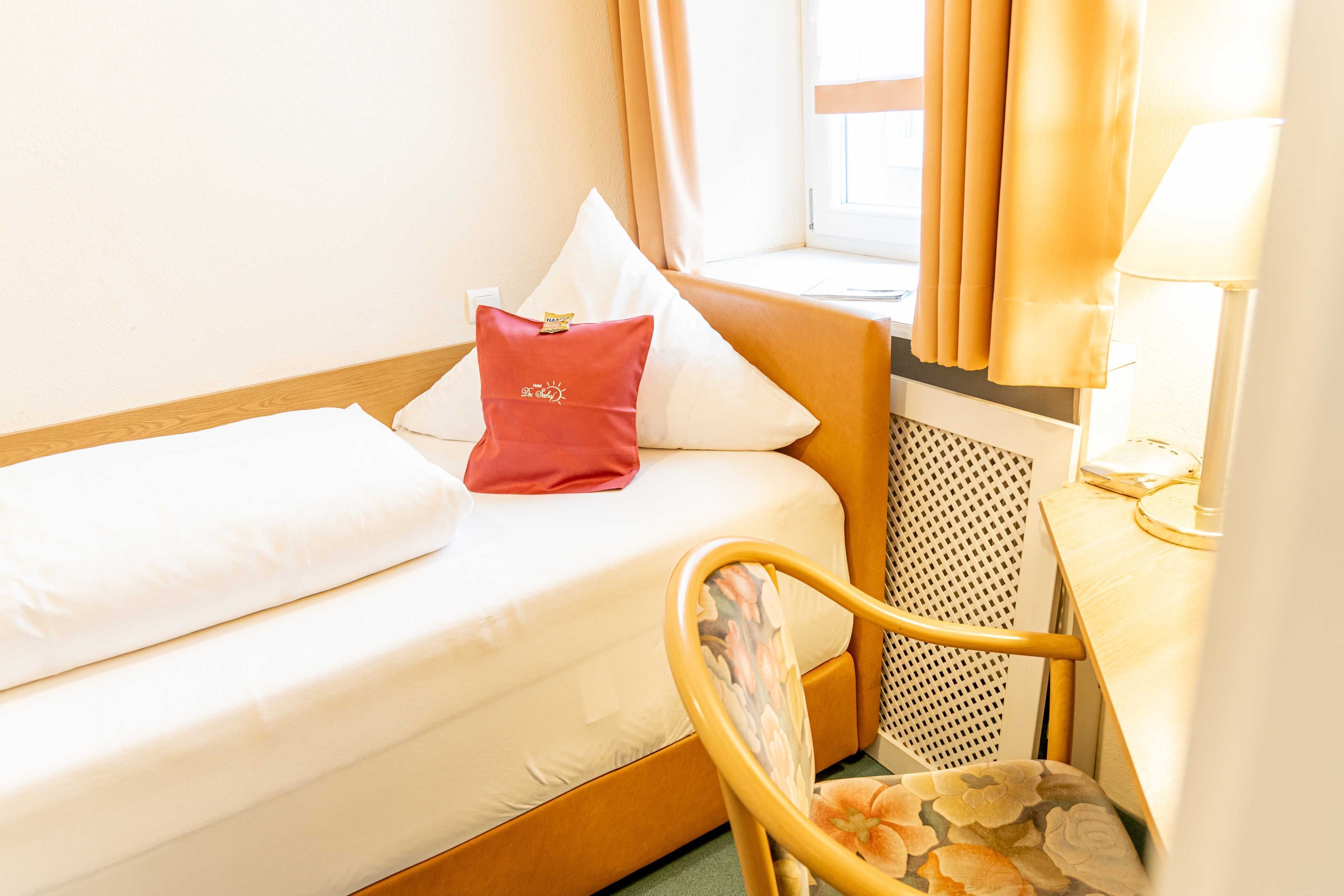 Une chambre d’hôtel avec un lit, une chaise, une lampe et une fenêtre avec des rideaux.