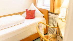 Ein Hotelzimmer mit Bett, Sessel, Lampe und einem fenster mit Vorhängen.