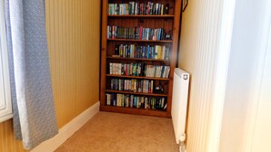 A corner room with a bookshelf filled with books, a radiator, and a patterned curtain.
