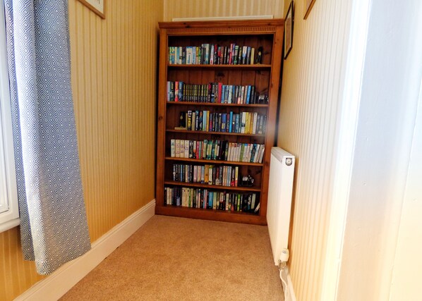 A corner room with a bookshelf filled with books, a radiator, and a patterned curtain. - The Old Gun Room (Ellesmere)