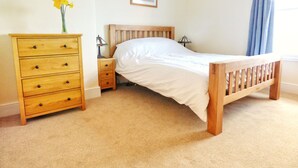 A bedroom with a wooden bed, a wooden dresser with drawers, a nightstand, a lamp, and a framed picture on the wall.