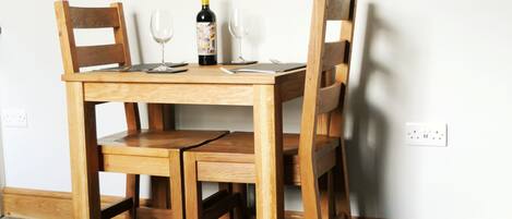 A wooden dining table with two chairs, a wine bottle, and two wine glasses.
