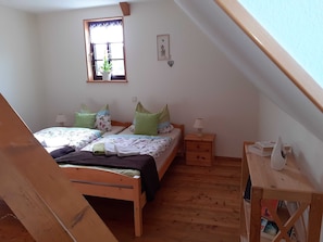 Une chambre avec deux lits, une fenêtre avec une plante, un plancher en bois et une petite table de chevet avec une lampe.