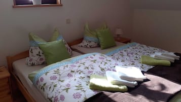 A bedroom with two beds, green pillows, floral bedspreads, a window with a plant, and a wall-mounted light.