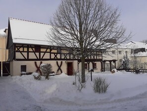 Un edificio tradicional con entramado de madera, techo cubierto de nieve y un pequeño árbol en primer plano.