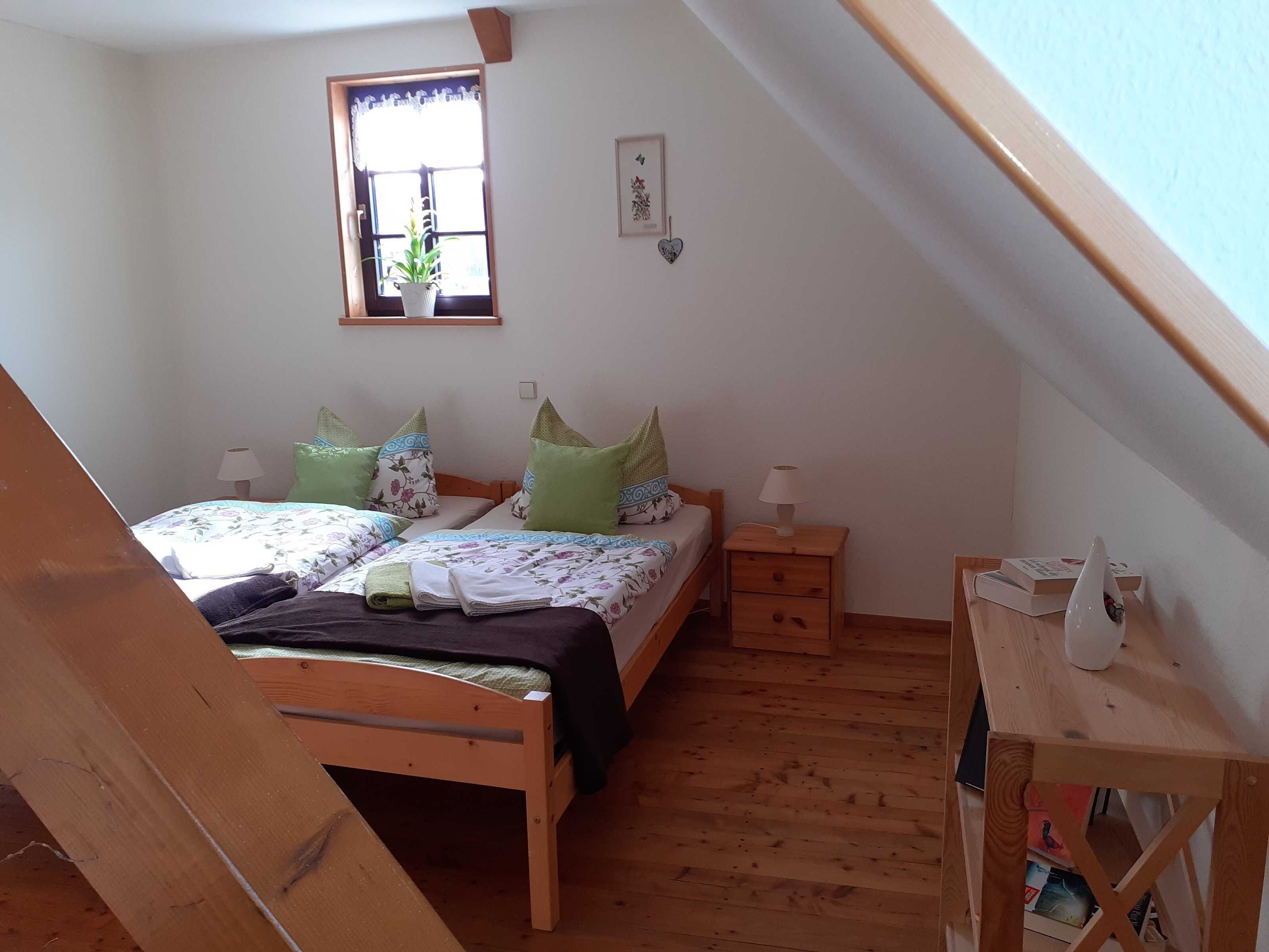 Ein Schlafzimmer mit zwei Betten, einem Fenster mit Pflanze, einem Holzboden und einem kleinen Nachttisch mit Lampe.