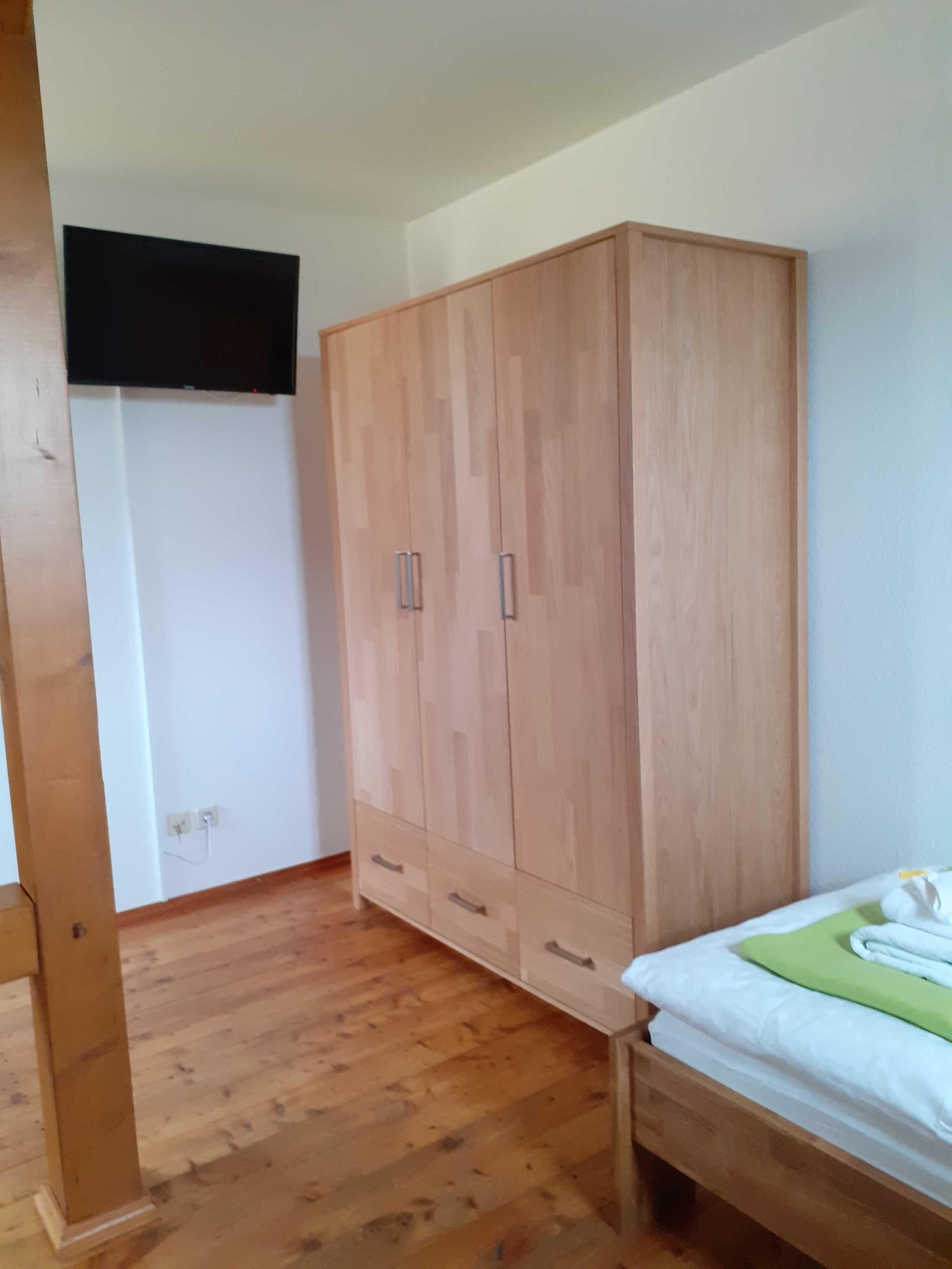 Ein Zimmer mit einem Holzschrank, einem Bett mit grüner Decke und einer weißen Wand.