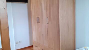 A room with a wooden wardrobe, a bed with a green blanket, and a white wall.