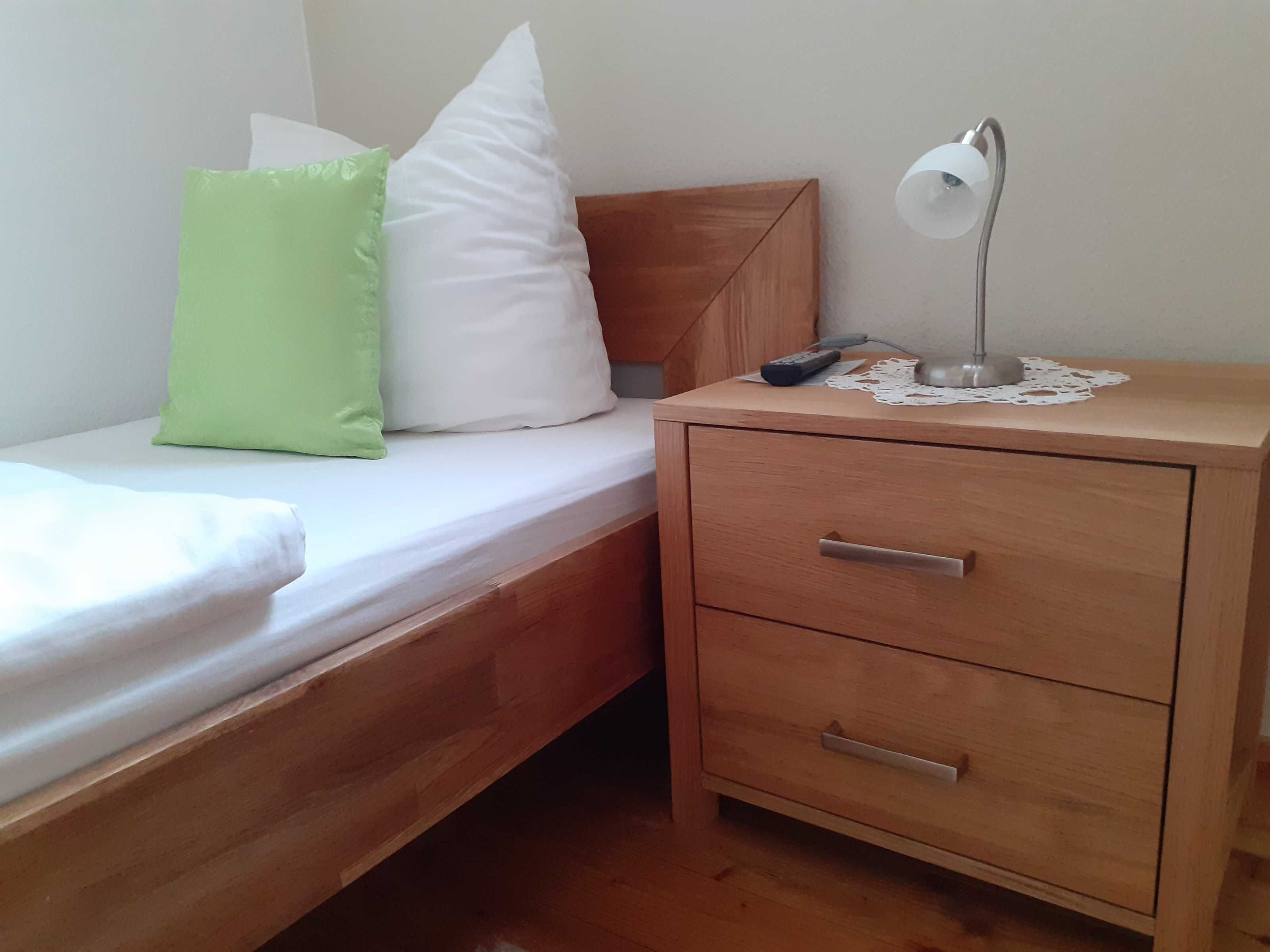Un lit simple avec des oreillers, une table de chevet avec une lampe et un tiroir.