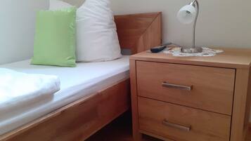 Un lit simple avec des oreillers, une table de chevet avec une lampe et un tiroir.