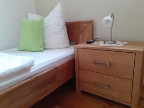 A single bed with pillows, a bedside table with a lamp, and a drawer.