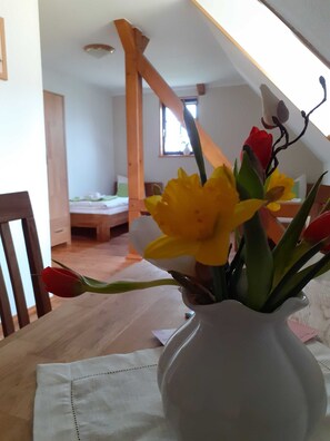 Una habitación con techo de madera, una cama, una ventana y un jarrón con flores sobre una mesa.