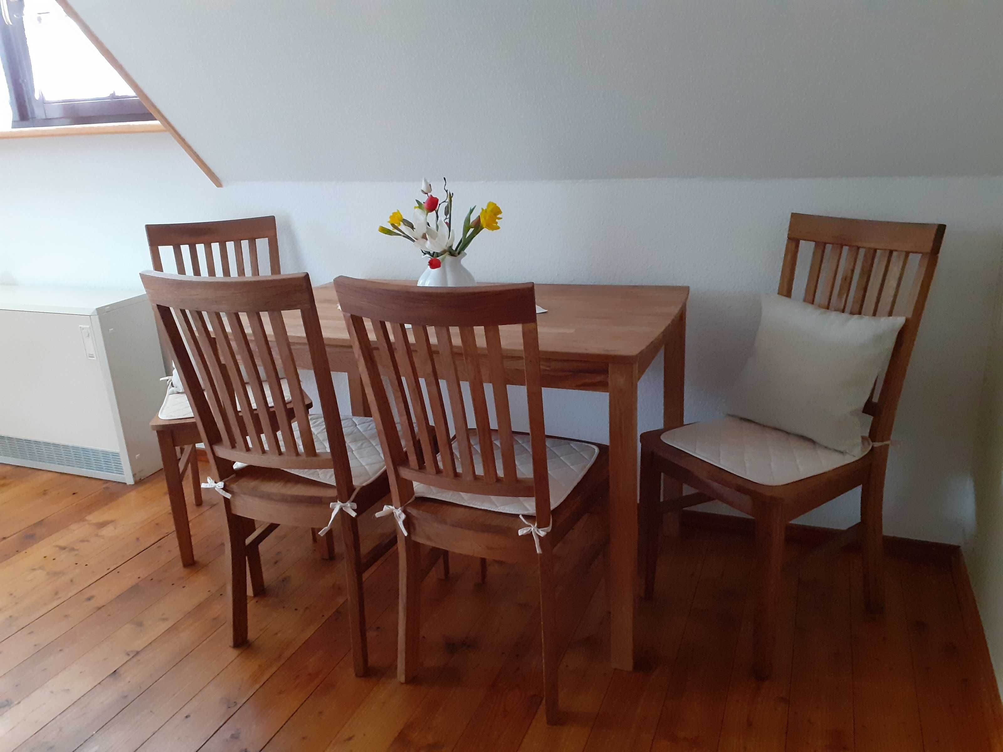 A dining area with a wooden table and chairs, a vase with flowers, and a window with a view.