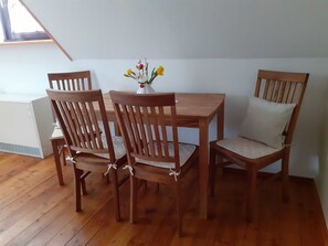 A dining area with a wooden table and chairs, a vase with flowers, and a window with a view.